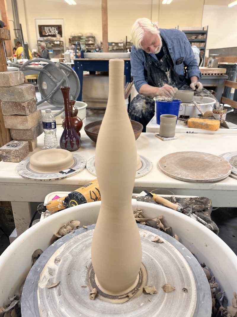 A tall bottle on the wheel in a busy studio.