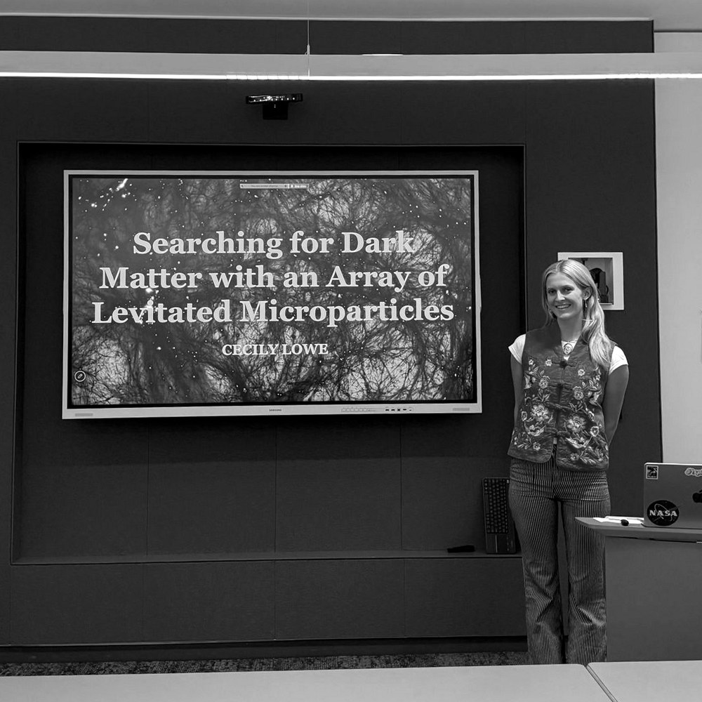 Cecily Lowe beside her prospectus title slide, Searching for Dark Matter with an Array of Levitated Microparticles.
